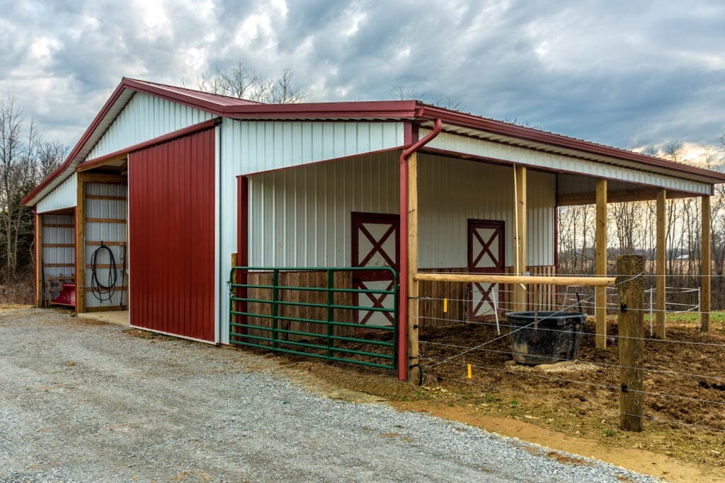 white and red trimmed with red metal roof 20x30 agricultural pole barn by tree