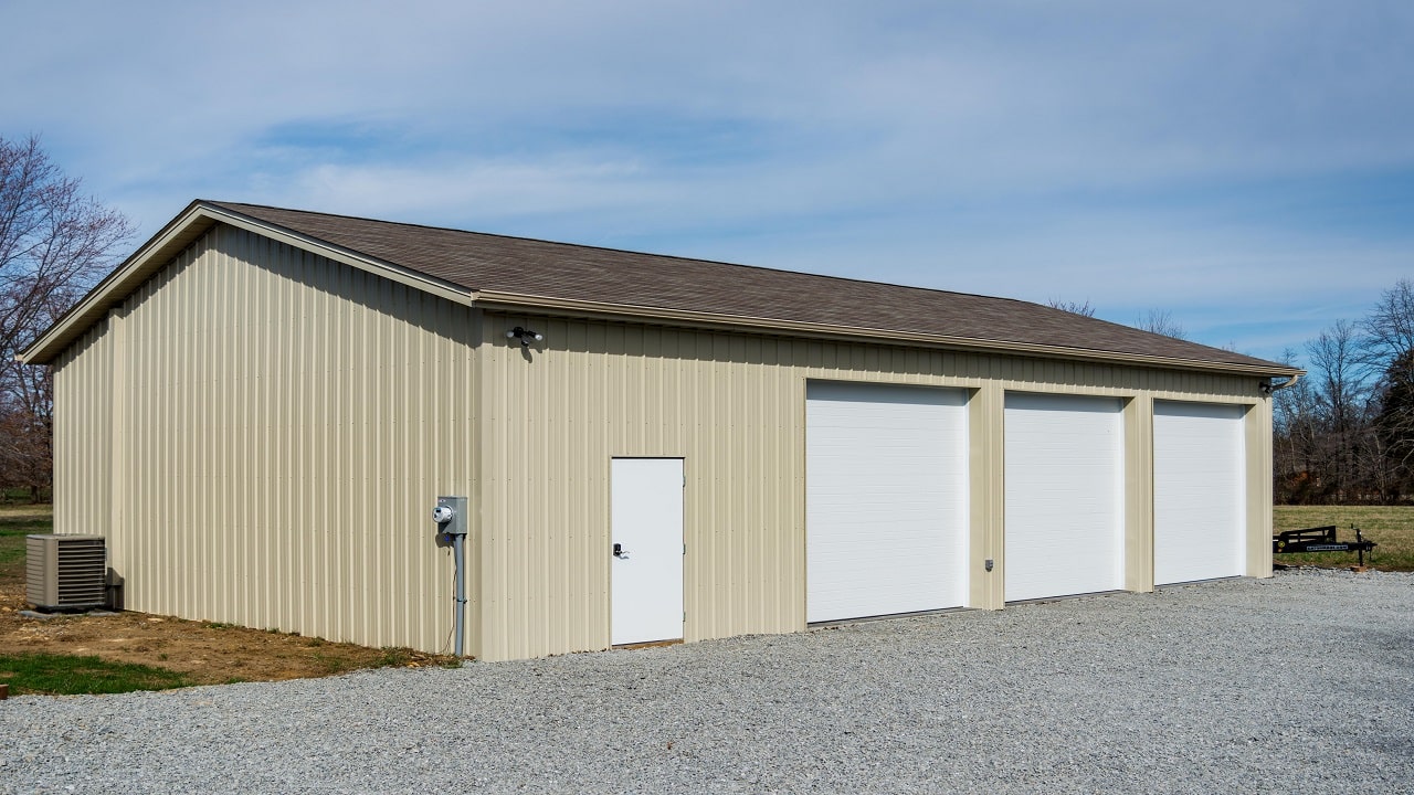 30x33 pole barn garage with light yellow metal siding, three white garage doors, and a brown roof