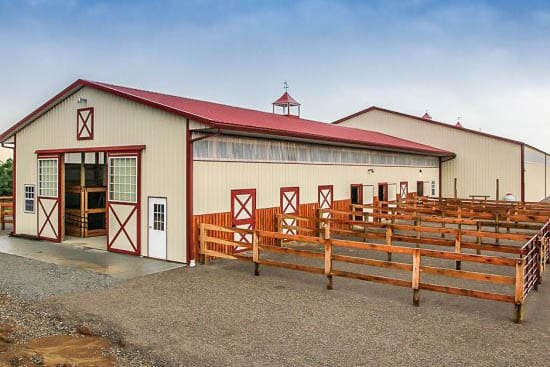 A 30x40 equestrian pole barn with tan siding, red trim and a red roof