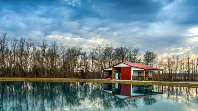 A 30x40 equestrian pole barn with a red roof standing right by a lake