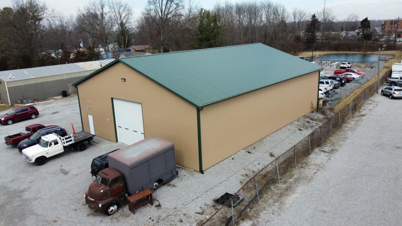A tan 60x100 commercial pole barn with a green roof and trucks parked outside