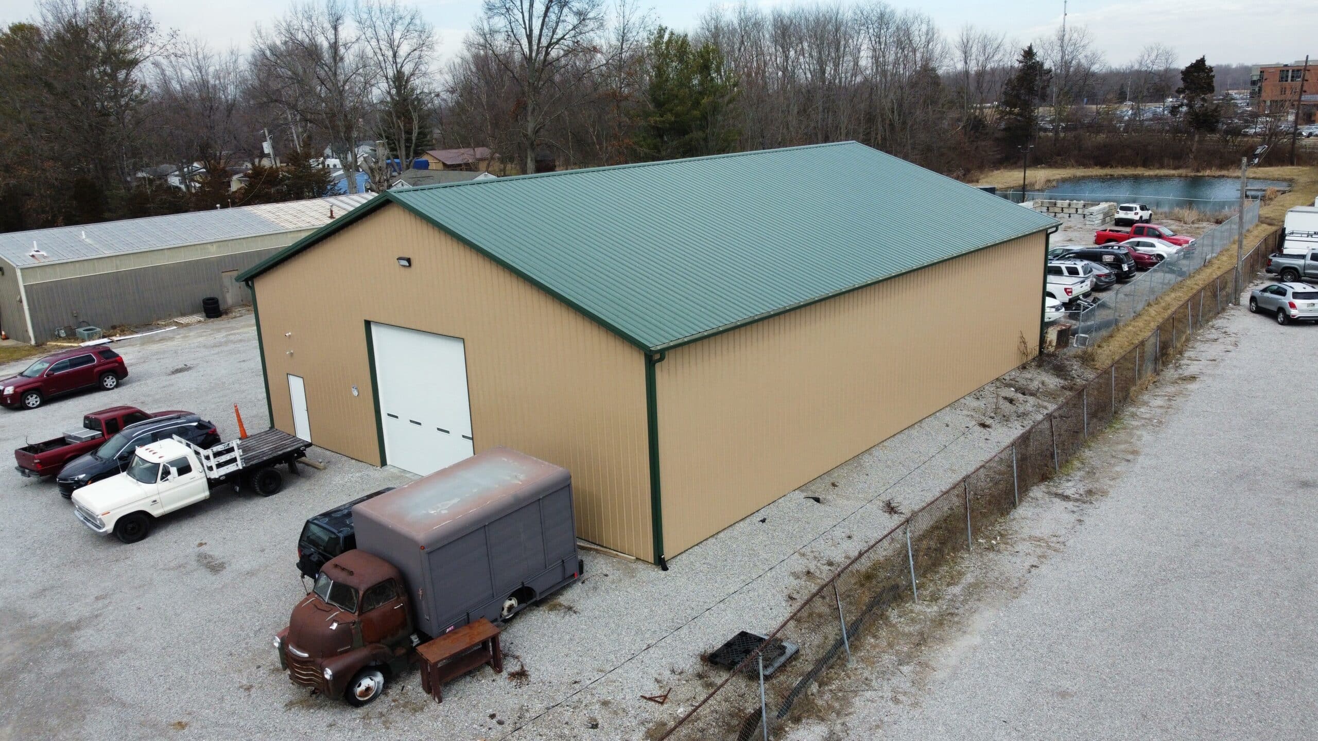 A tan 60x100 commercial pole barn with a green roof and trucks parked outside