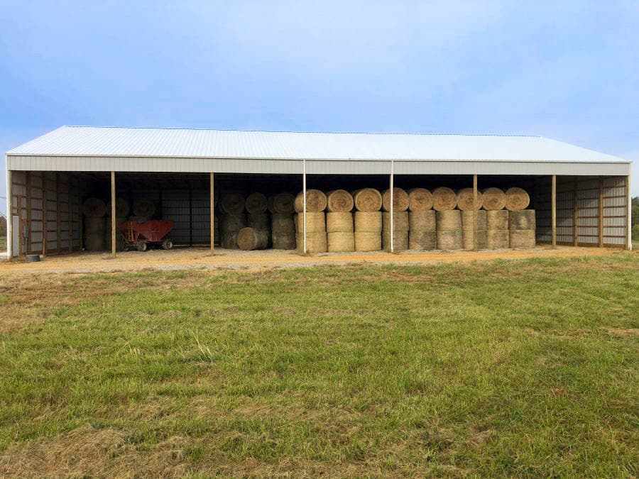 60x60 gray pole barn with open sides being used as hay storage