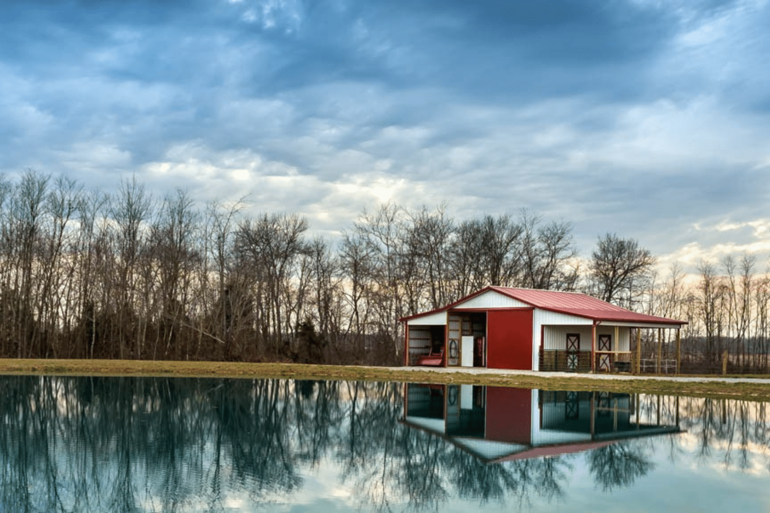 80x120 red and white equestrian pole barn kit by a pond