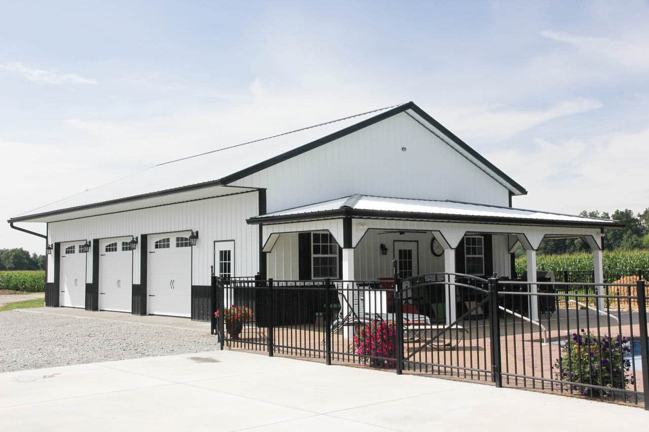 white 20x30 pole barn garage with black trim and three white garage doors with transom windows poolside