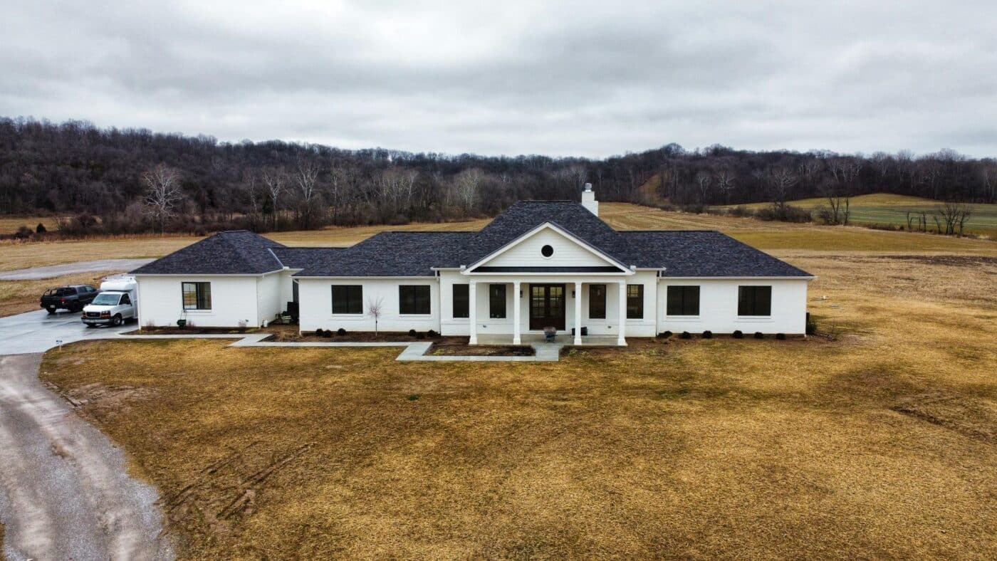 one-story white barndominium with a black shingle roof in a field near a road in Richmond IN