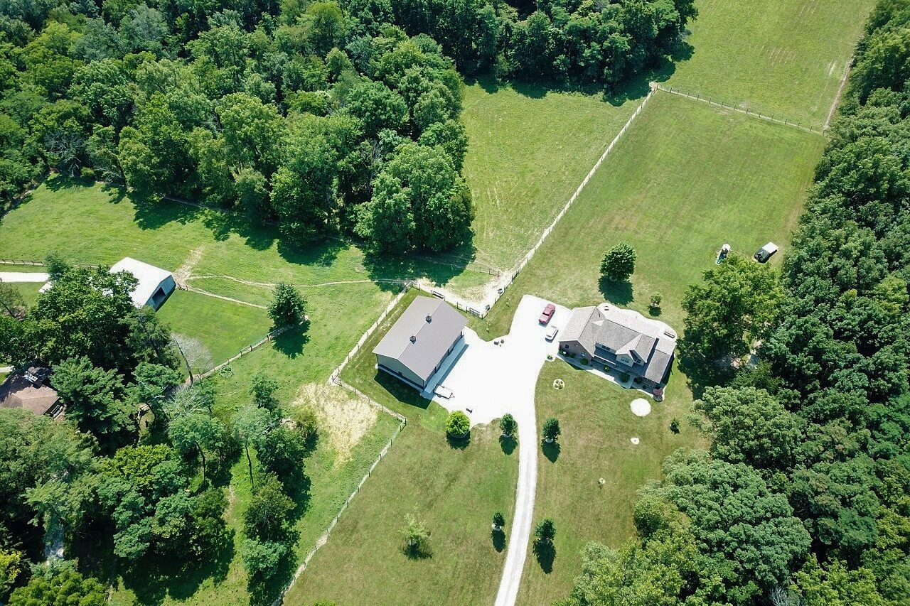 aerial view of a pole barn garage and barndominium on a property with a long winding driveway and a lot of green grass