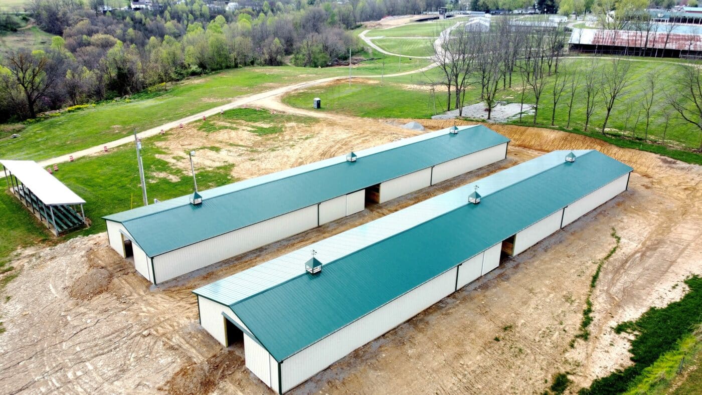 aerial view of tan and green equestrian pole barn with three cupolas on top of roof
