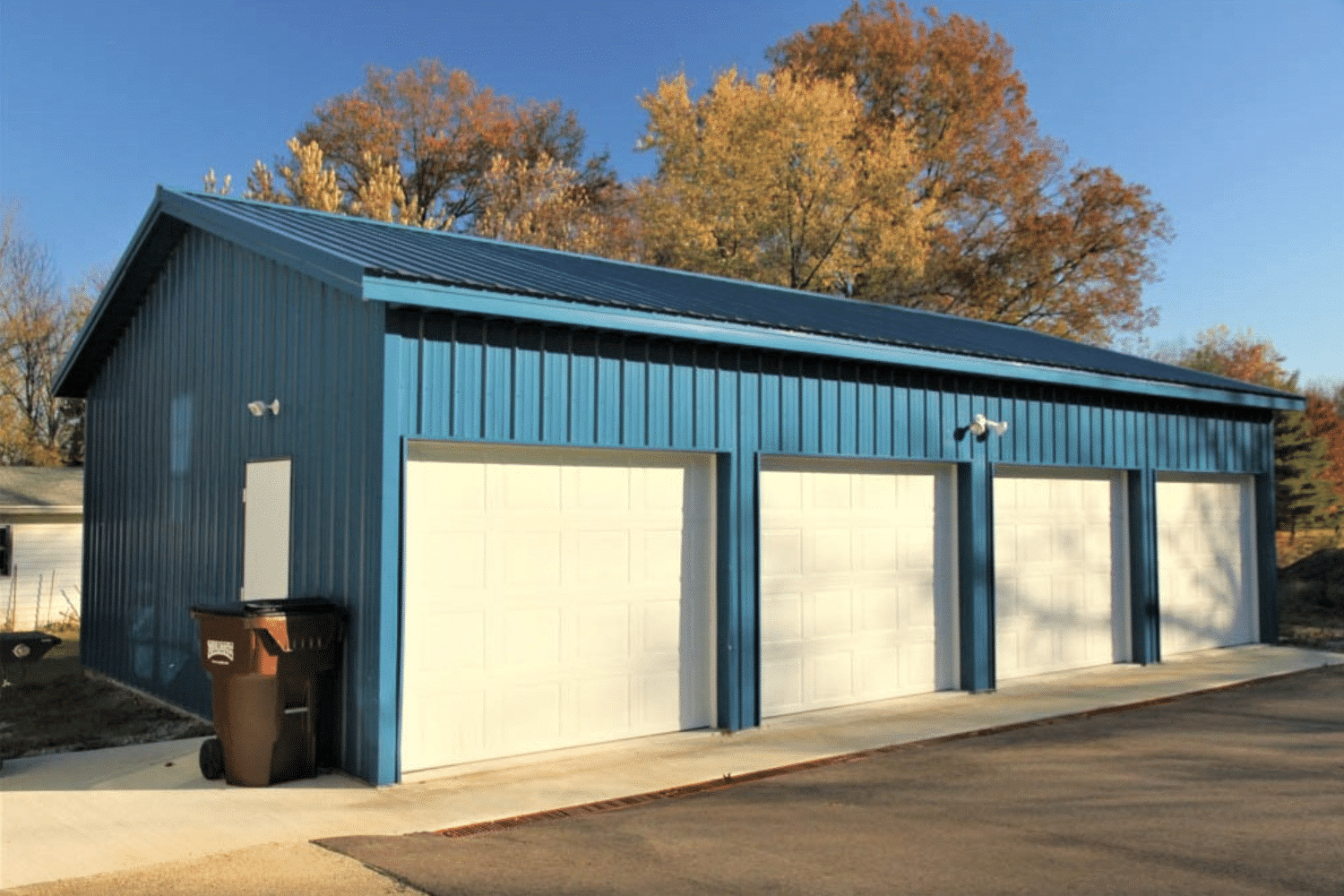 side angle of blue pole barn garage with 4 white overhead doors