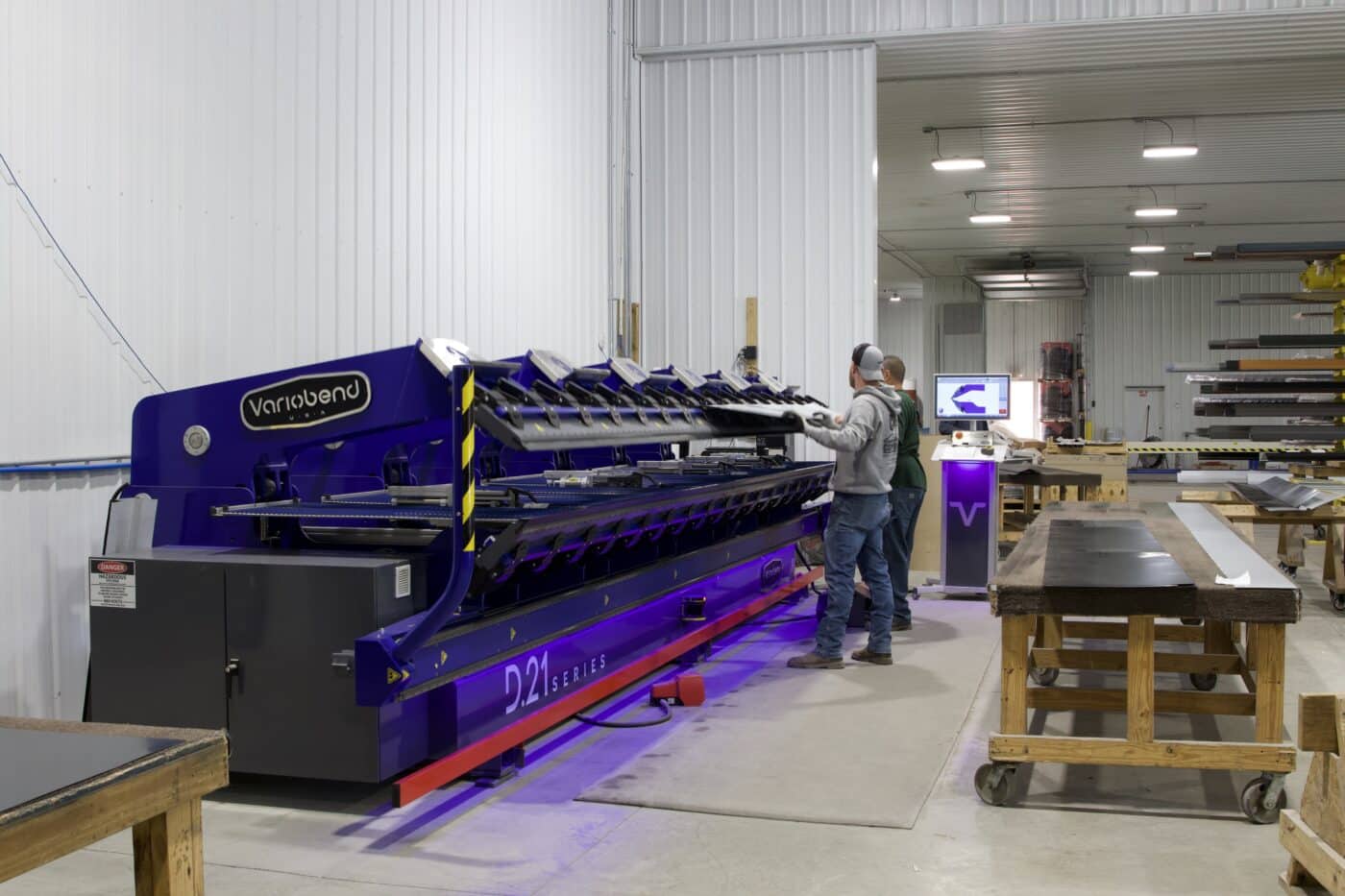 Men manufacturing metal sheets for 100x120 commercial pole barn kits using a large blue machine