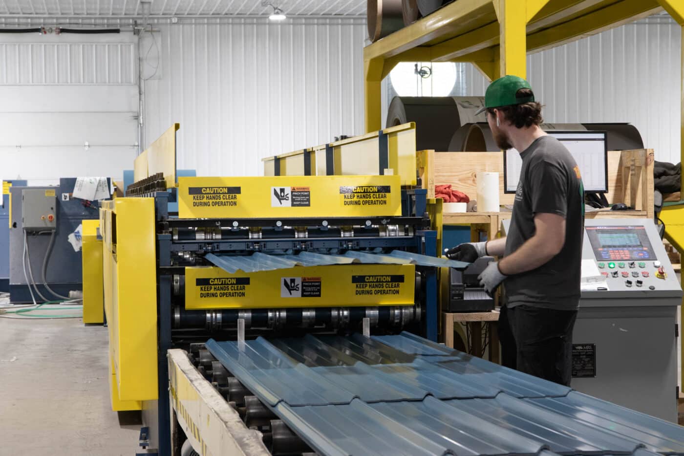 blue metal panels being manufactured by a man at a yellow machine