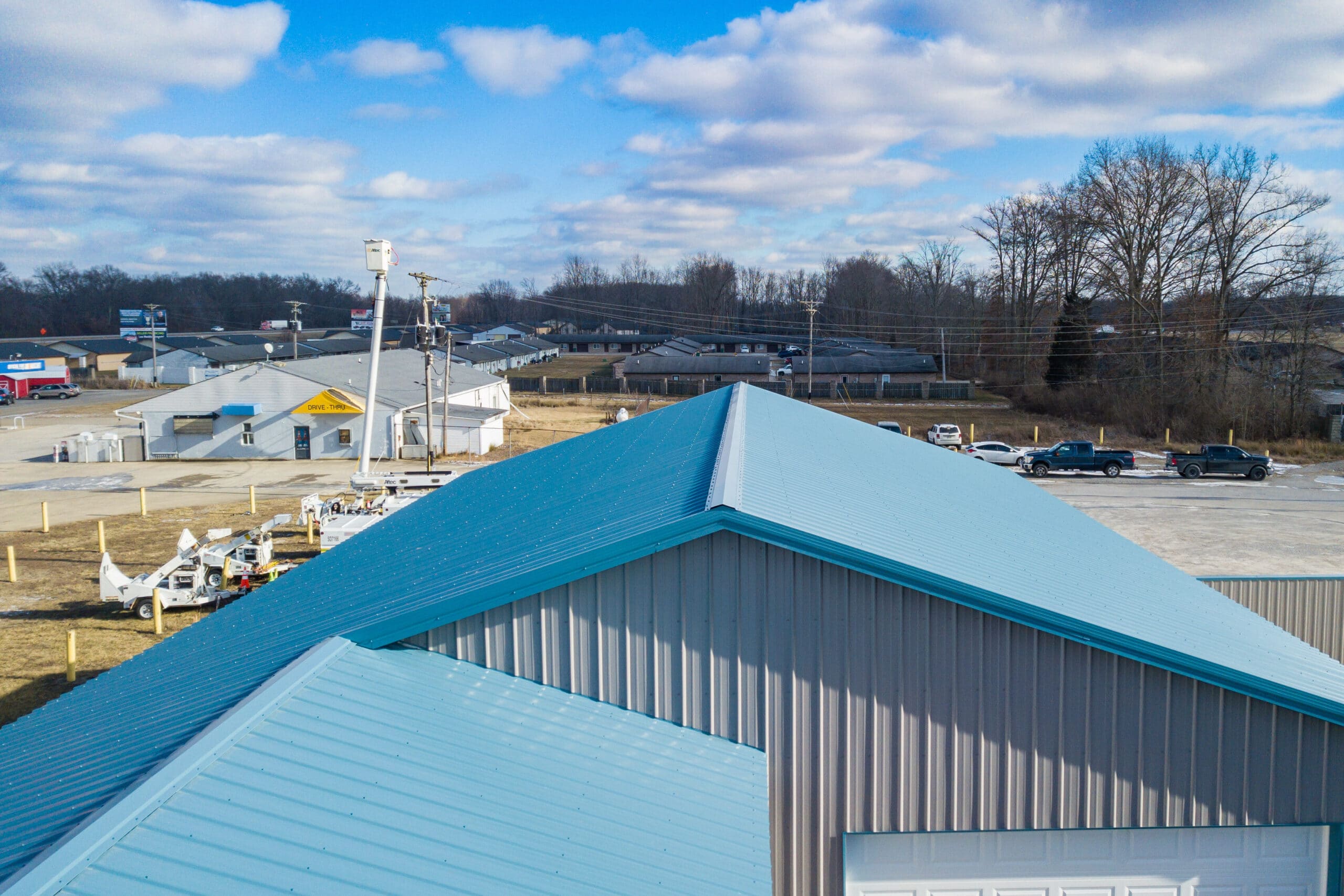 blue metal roofing panels on top of a gray sided metal pole barn garage with a white overhead garage door