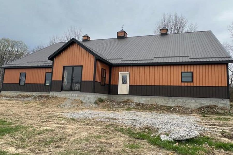 brown and orange commercial pole barn with stone foundation adn three cupolas on top of the metal roof
