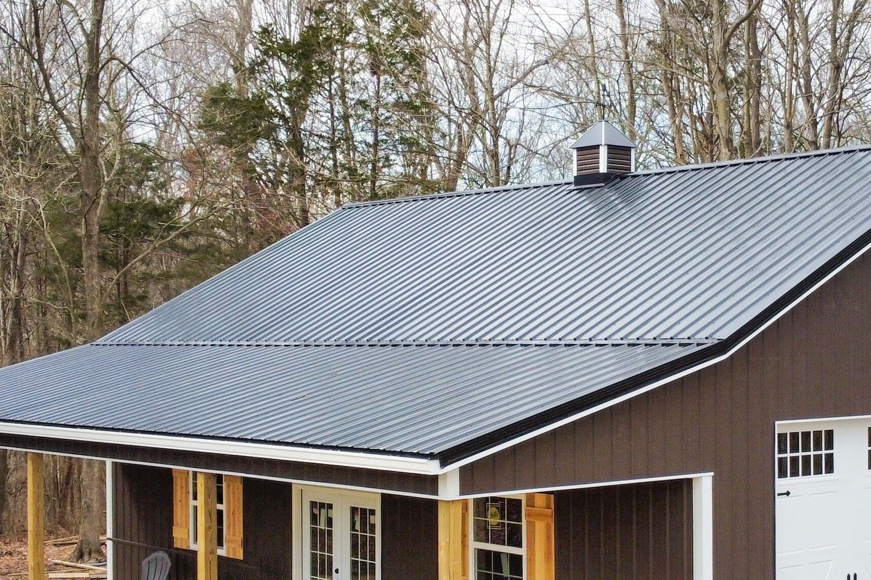 brown pole barn garage with two white overhead doors with transom windows on the side and a front porch with two doors and two windows