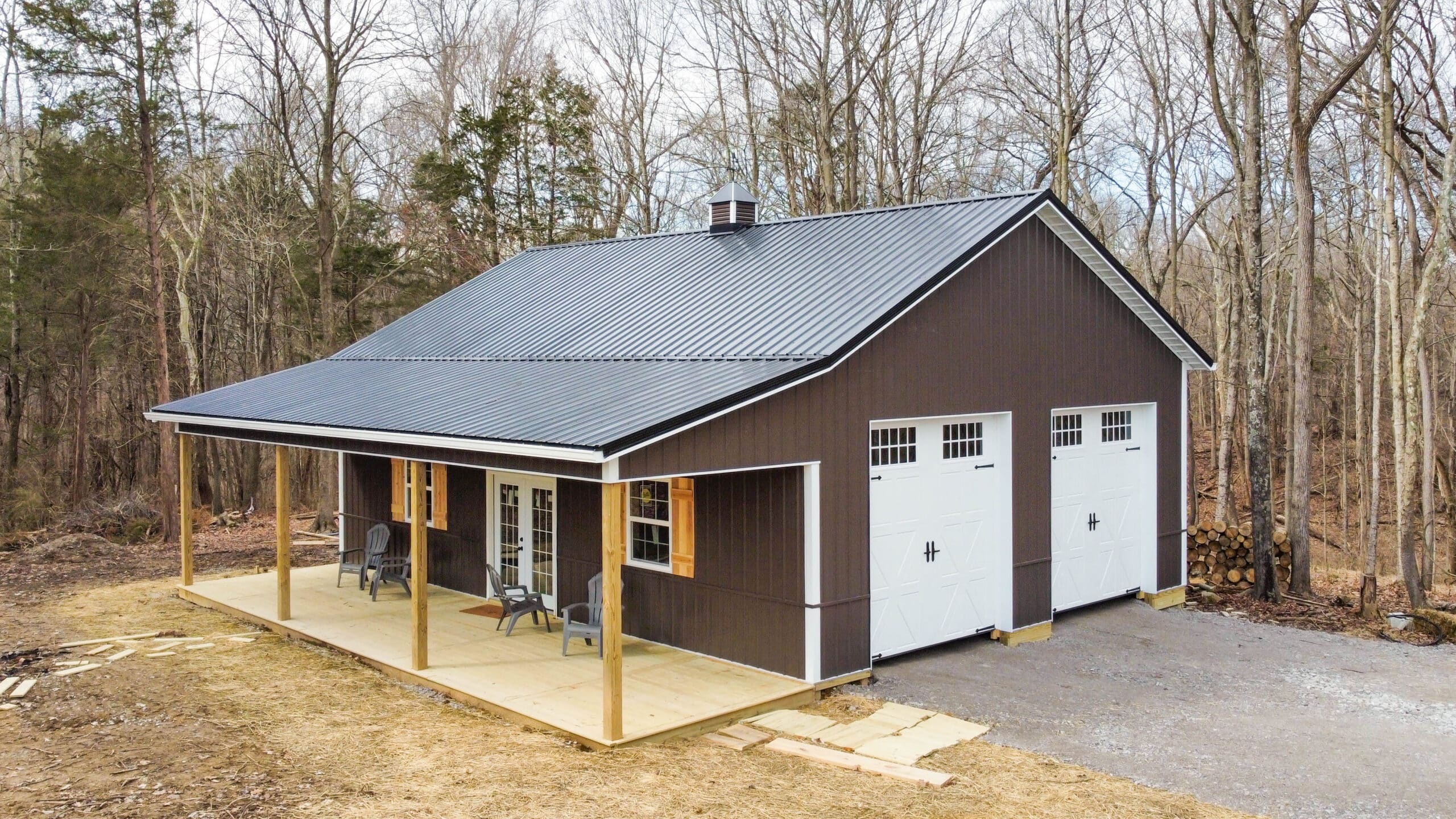 A brown pole barn garage with two white garage doors and a porch in Morrow OH