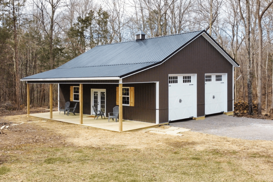 brown sided pole barn garage with black metal roof hanging over a porch featuring two white overhead doors on the side with transom windows