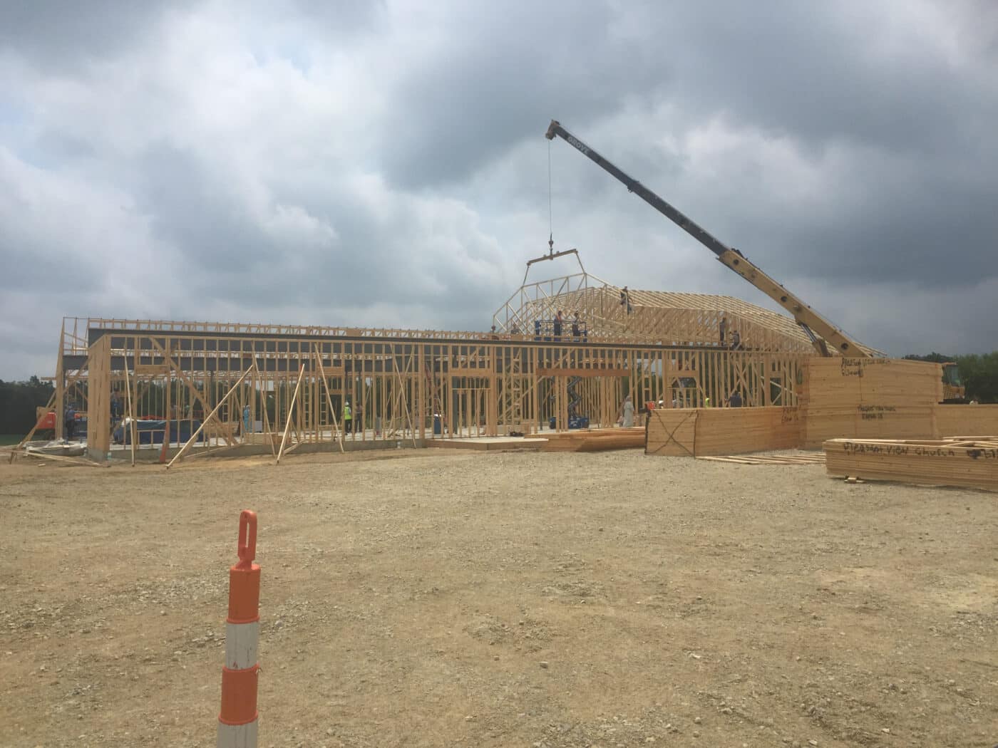 crane lowering a wooden roof truss onto a pole barn frame with multiple men on the roof helping to put it in place