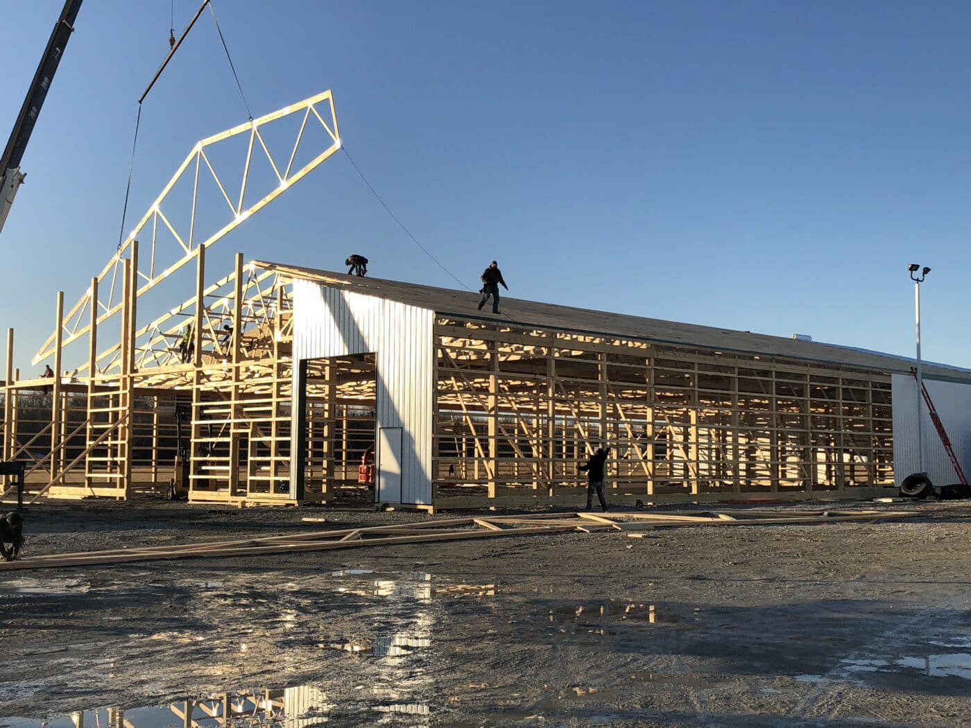 A crane lowering a roof truss onto a 60x100 commercial pole barn under construction