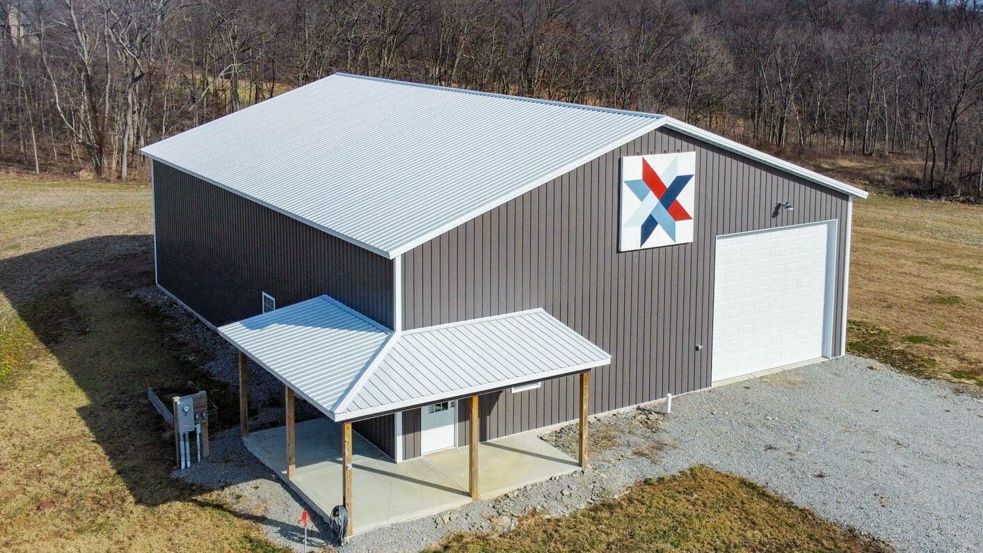 gray 50x60 commercial pole barn with light gray roof and one white garage door and a unique logo on top
