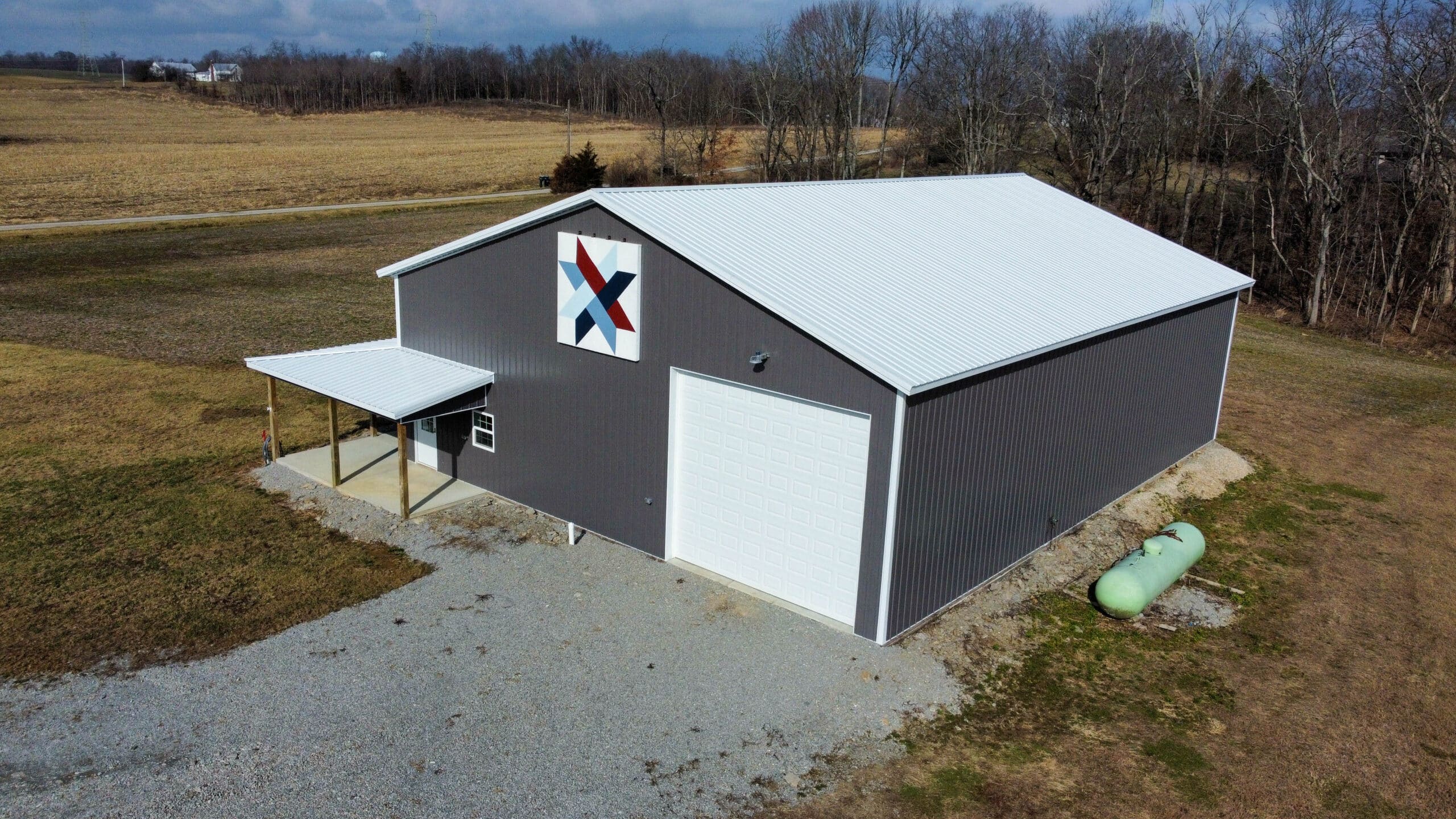 gray and white pole barn garage with one overhead door and side door with overhang