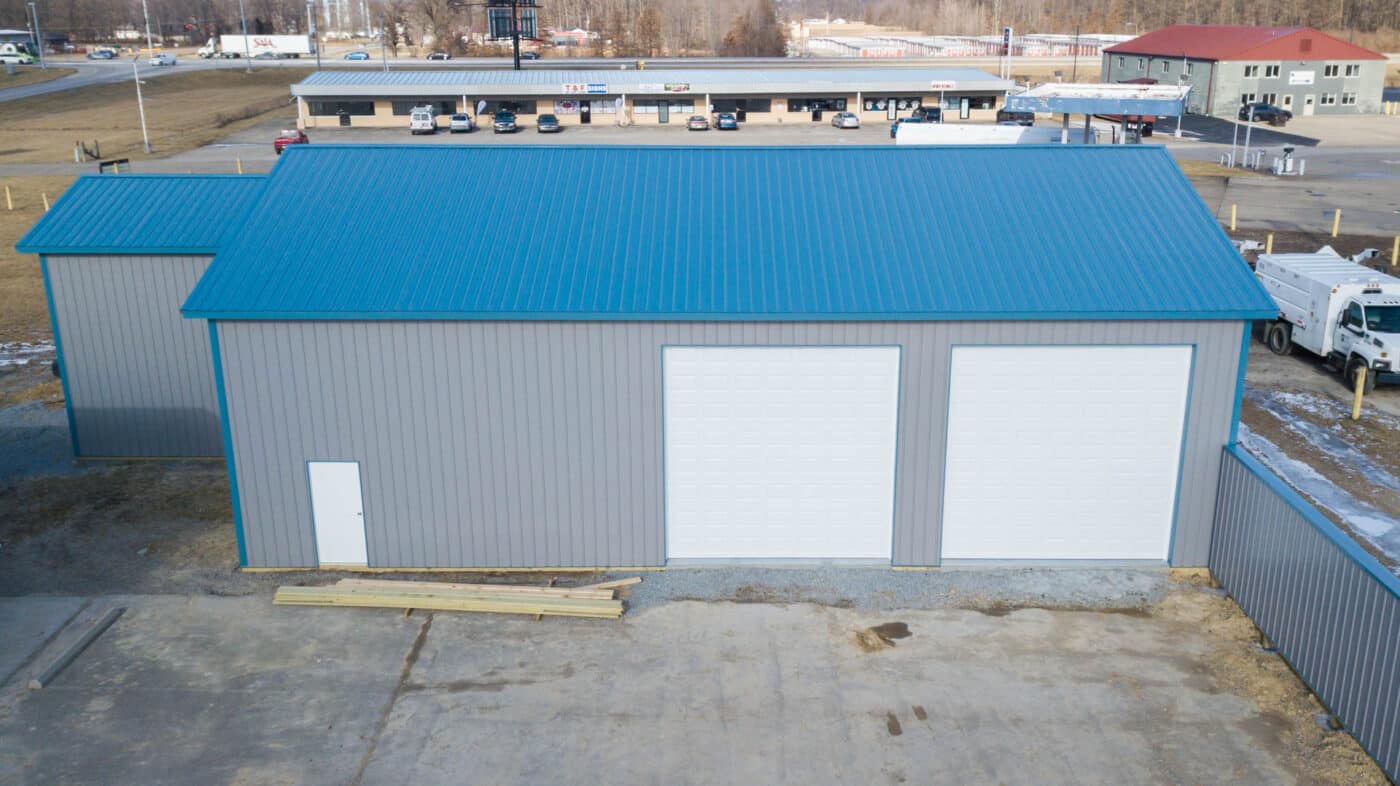 gray commercial pole barn with blue metal roof and two white garage doors