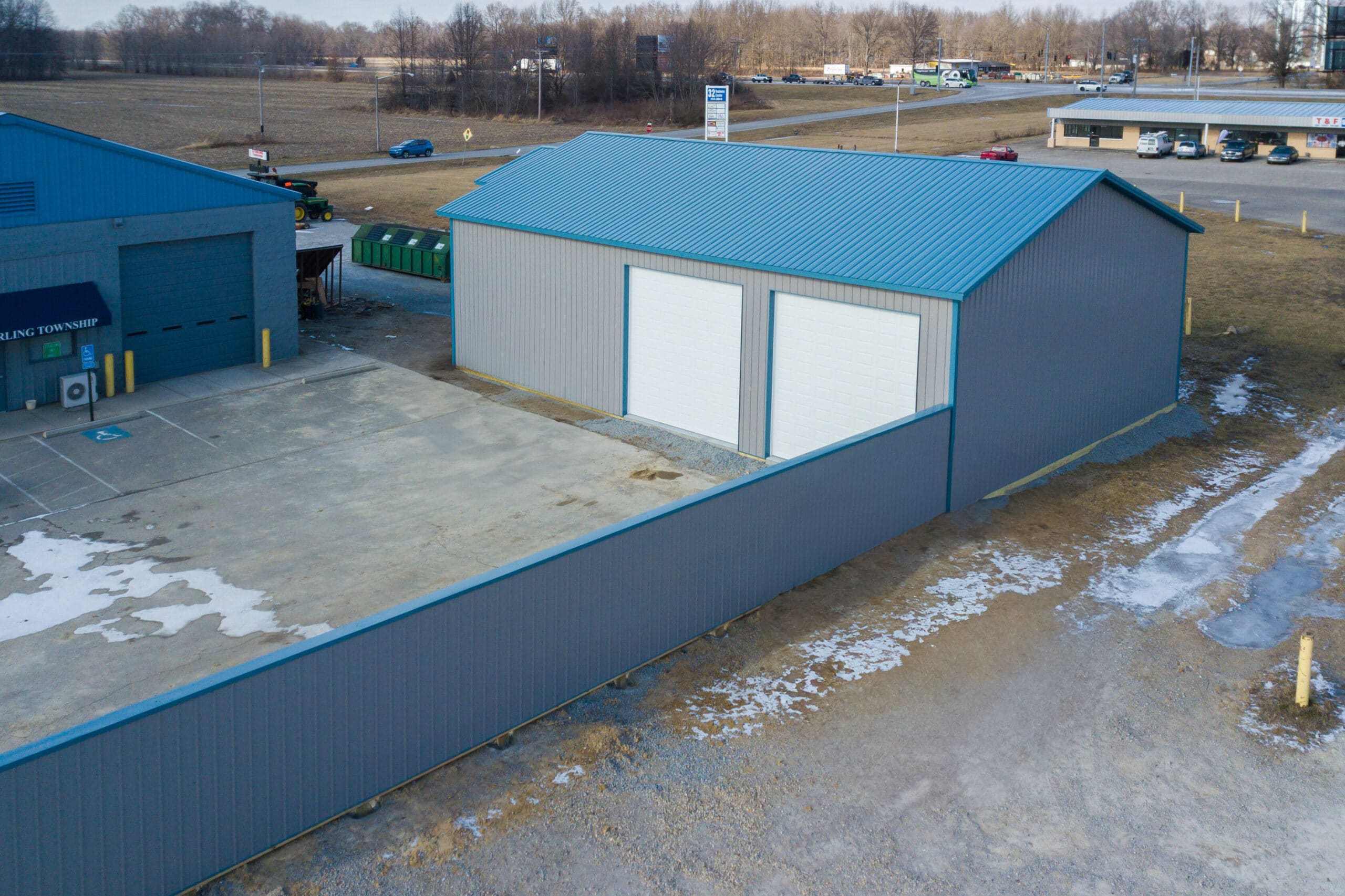 gray metal garage pole barn with blue metal trim and roofing plus two white overhead doors