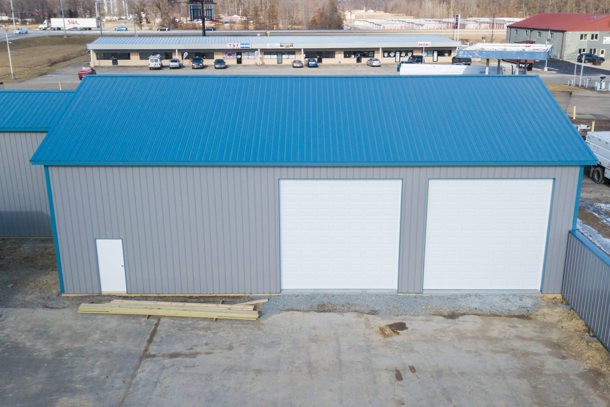 gray sided 24x40 pole barn garage with blue trim and metal roof featuring two white overhead doors and a white side door