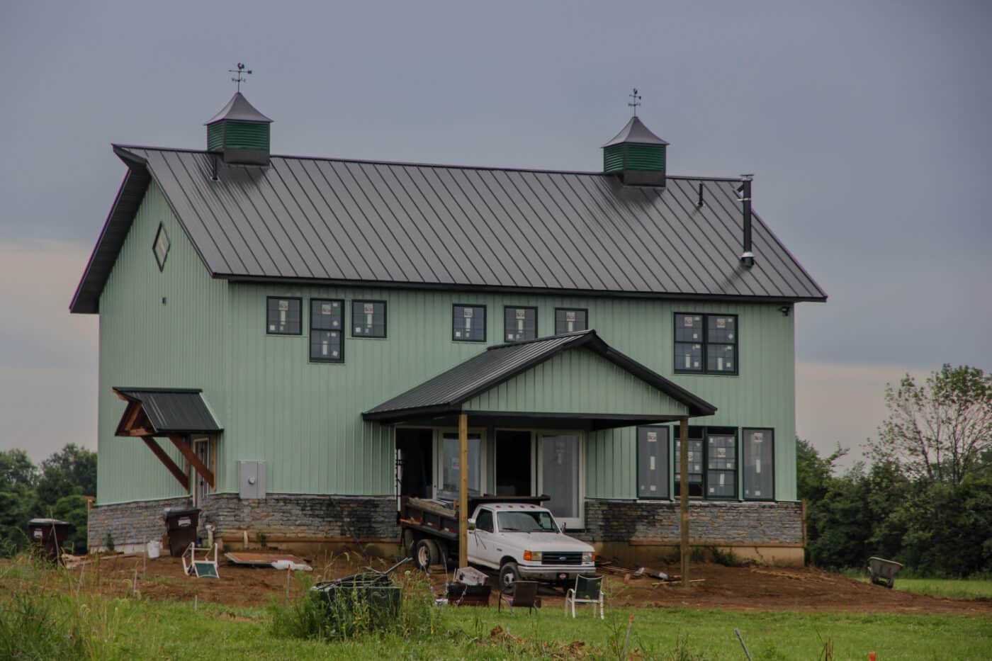 green 30x30 barndominium with black metal roof and stone detailing along the bottom featuring a side entrance with a black metal overhang and a front entrance with a black metal overhang