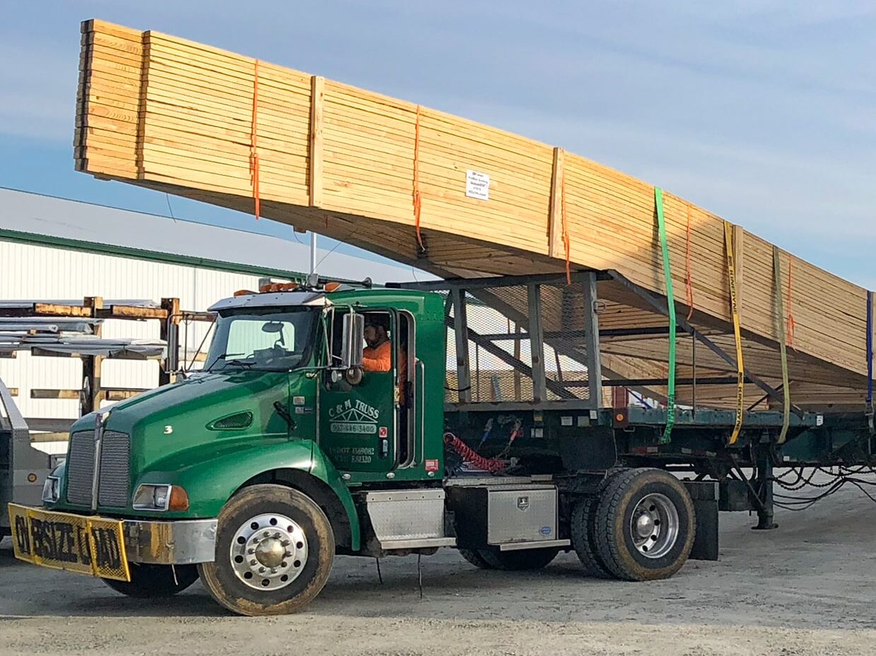 green CMT Components truck carrying wooden roof trusses for pole barn kits in Covington OH