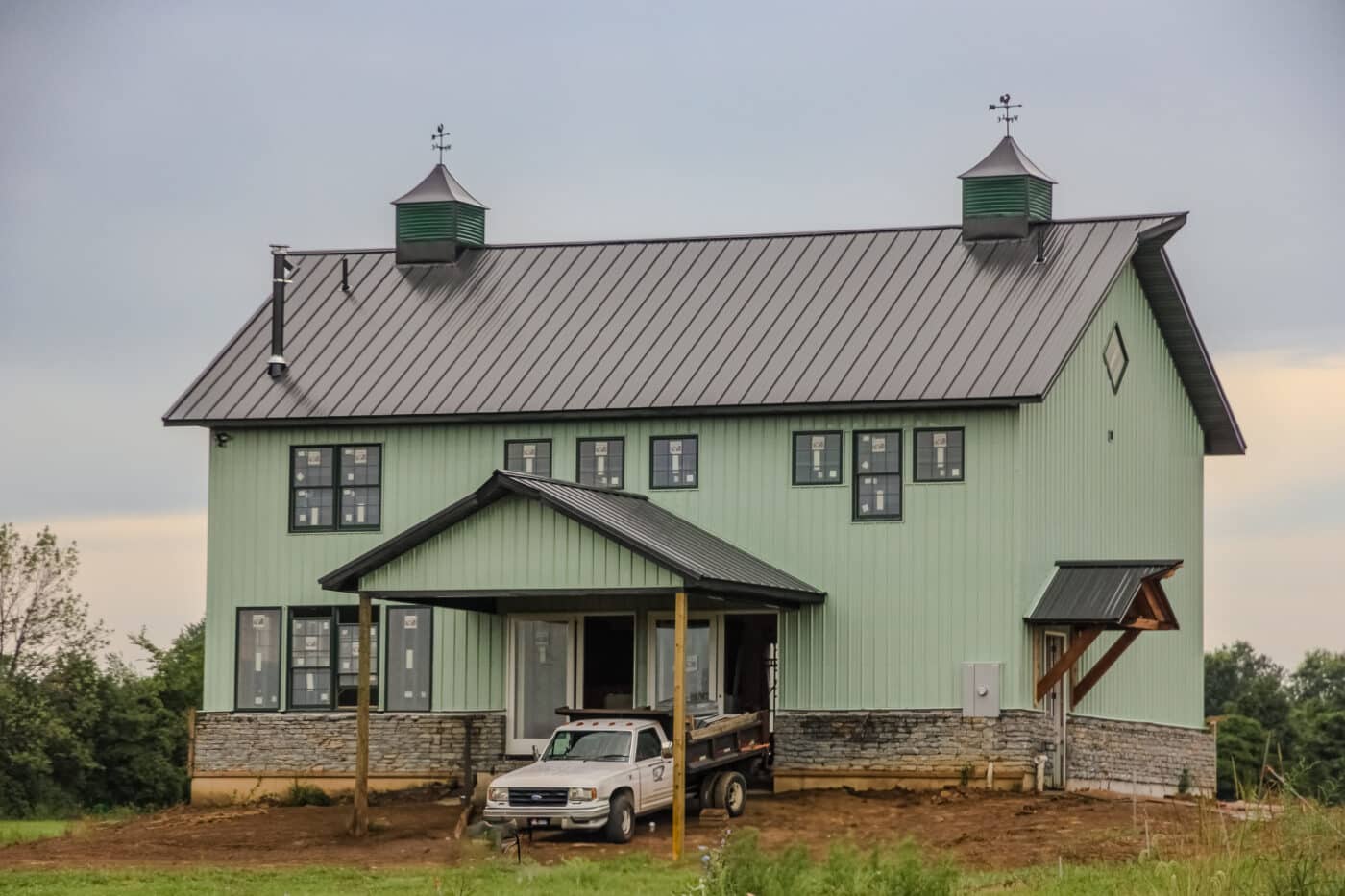 green barndominium with black metal roof and truck parked out front