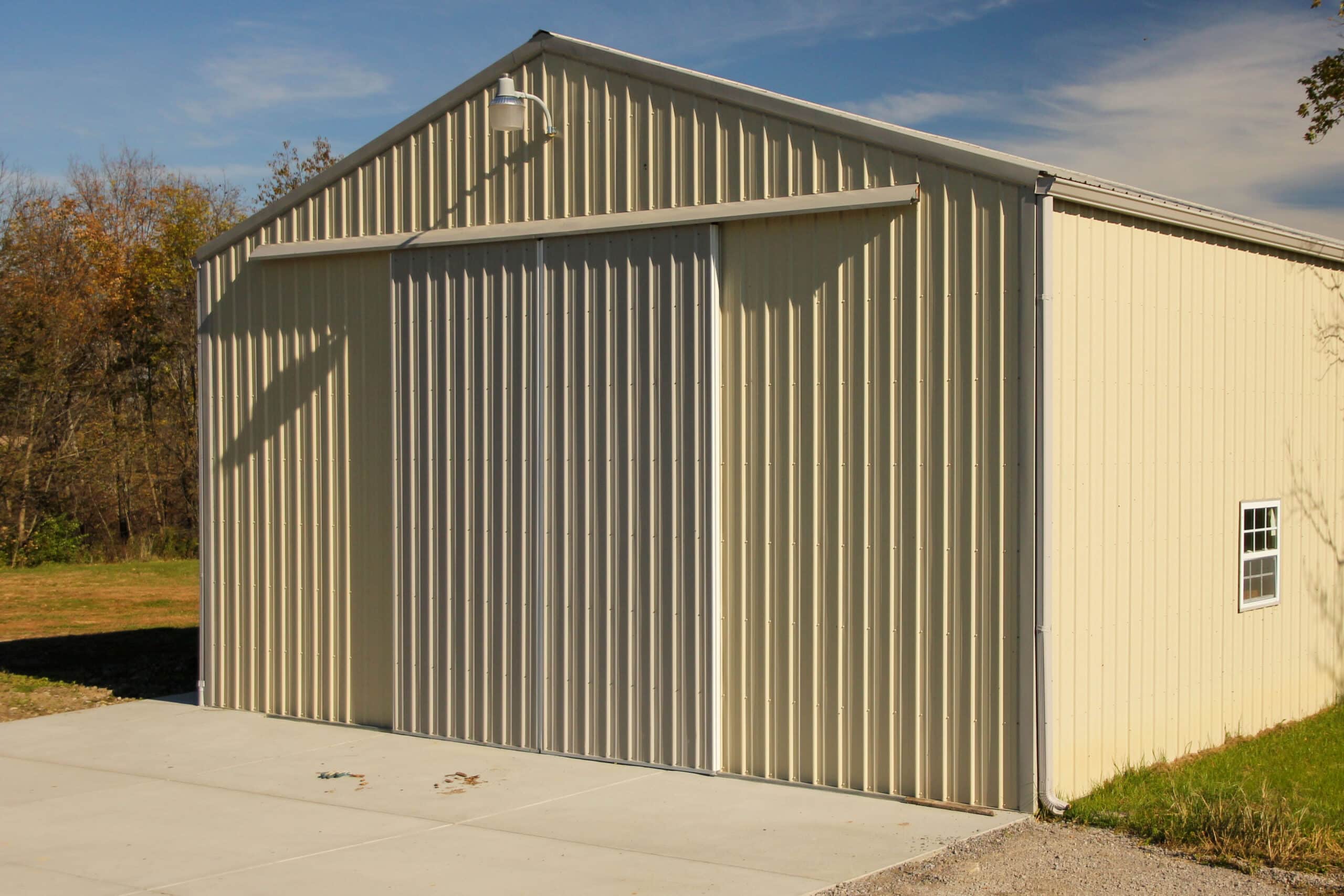 light yellow metal pole barn with white slider doors with light overtop and two windows on the right side