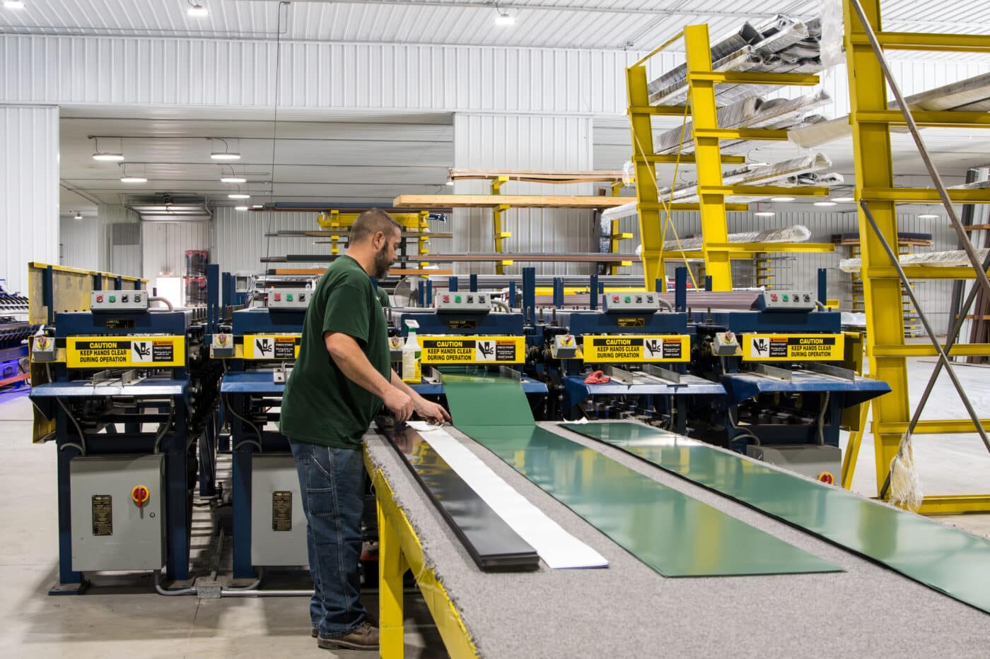man at blue and yellow machine manufacturing green metal panels for a 24x24 pole barn garage