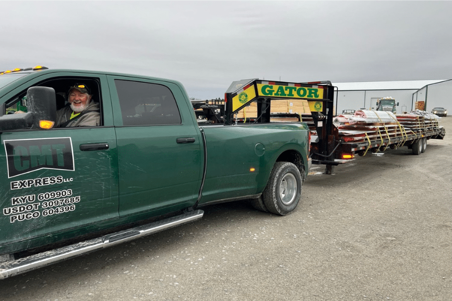 man in green truck with attached gooseneck trailer hauling components for a barndominium kit