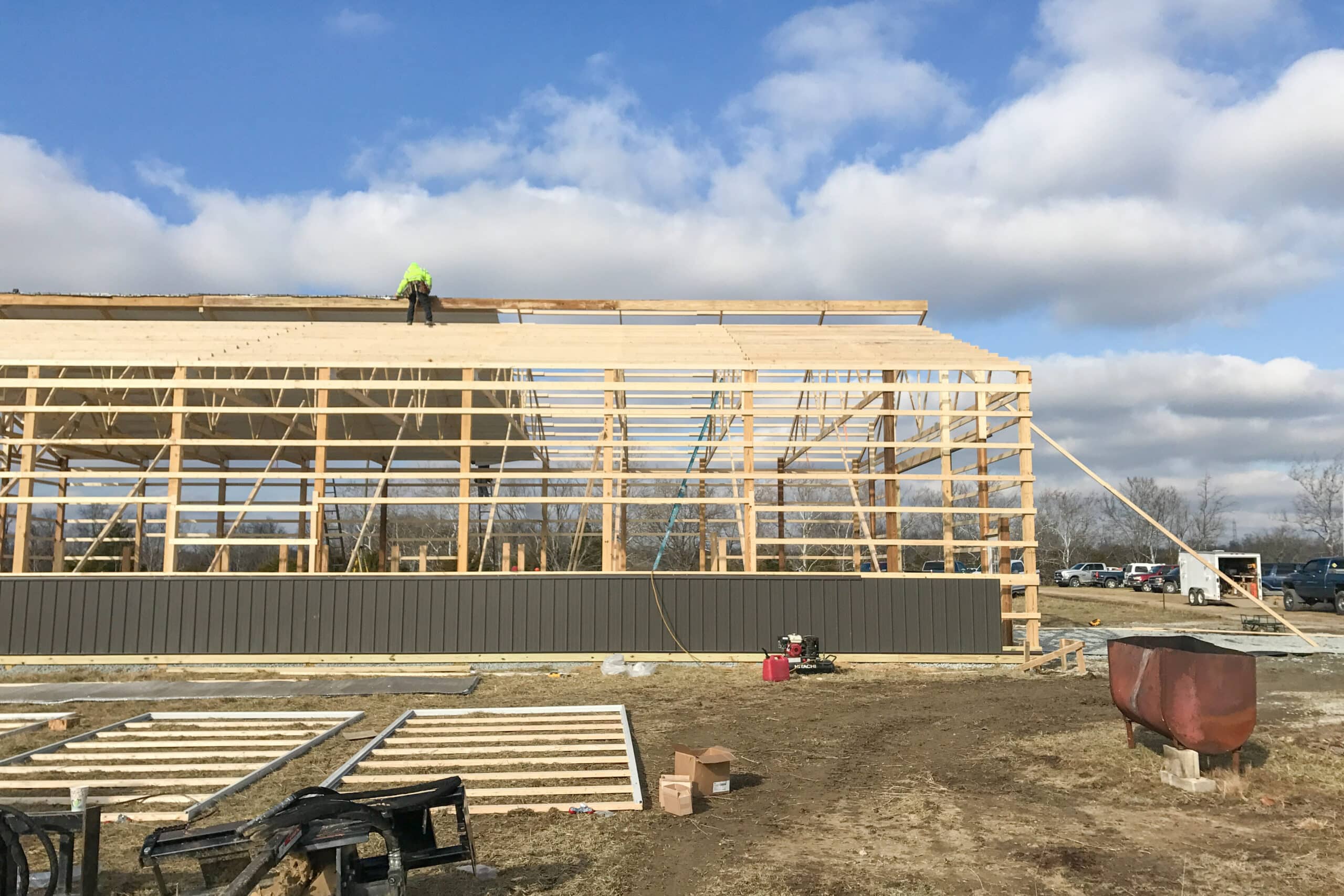 man laying metal roofing on top of wooden roof trusses
