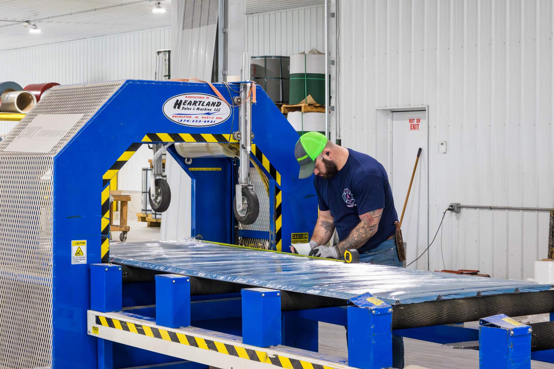 man manufacturing metal panels at blue machine for pole barn kit in New Richmond OH