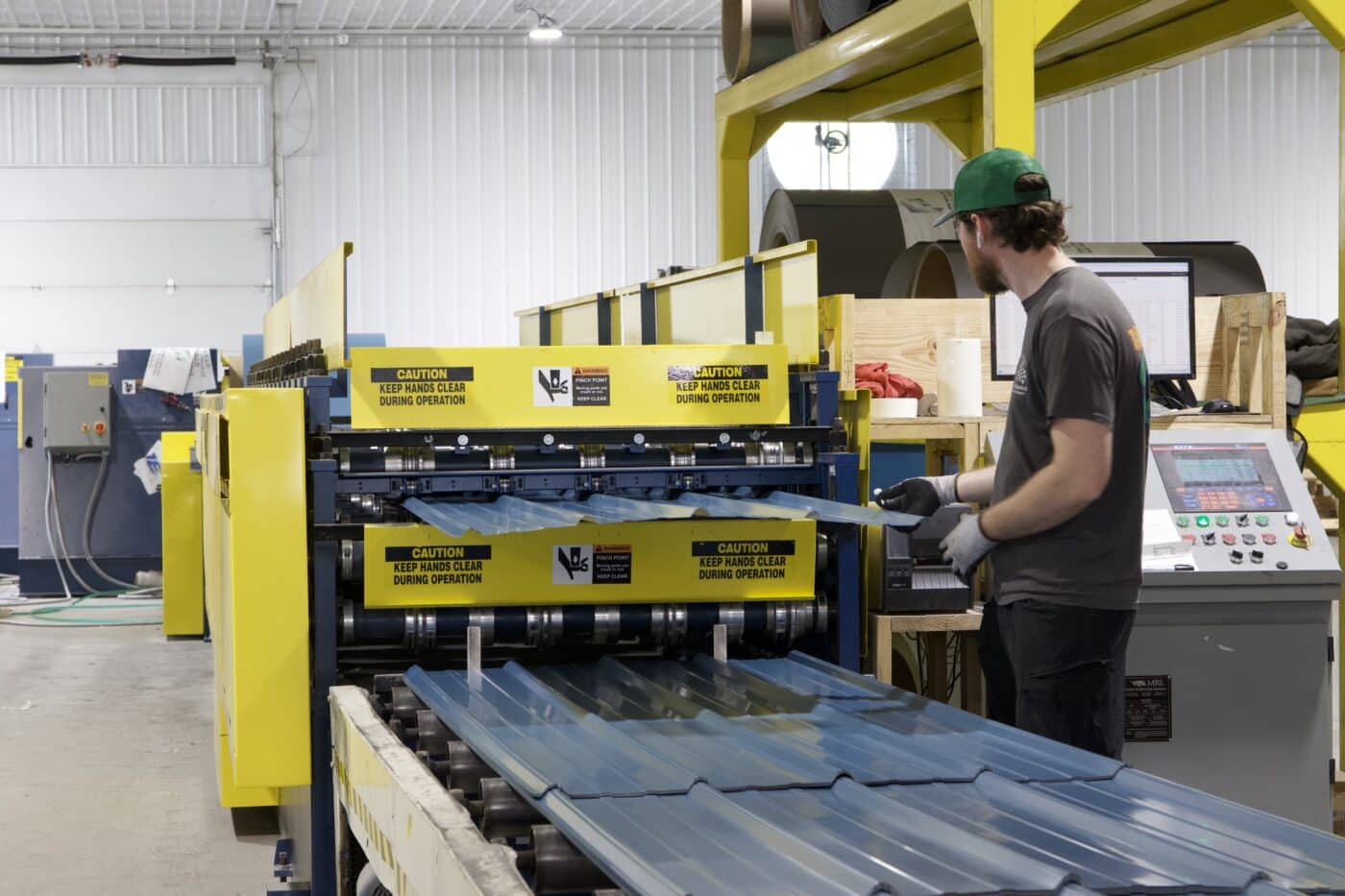 A man using yellow machinery to manufacture blue metal panels for a 60x100 commercial pole barn kit