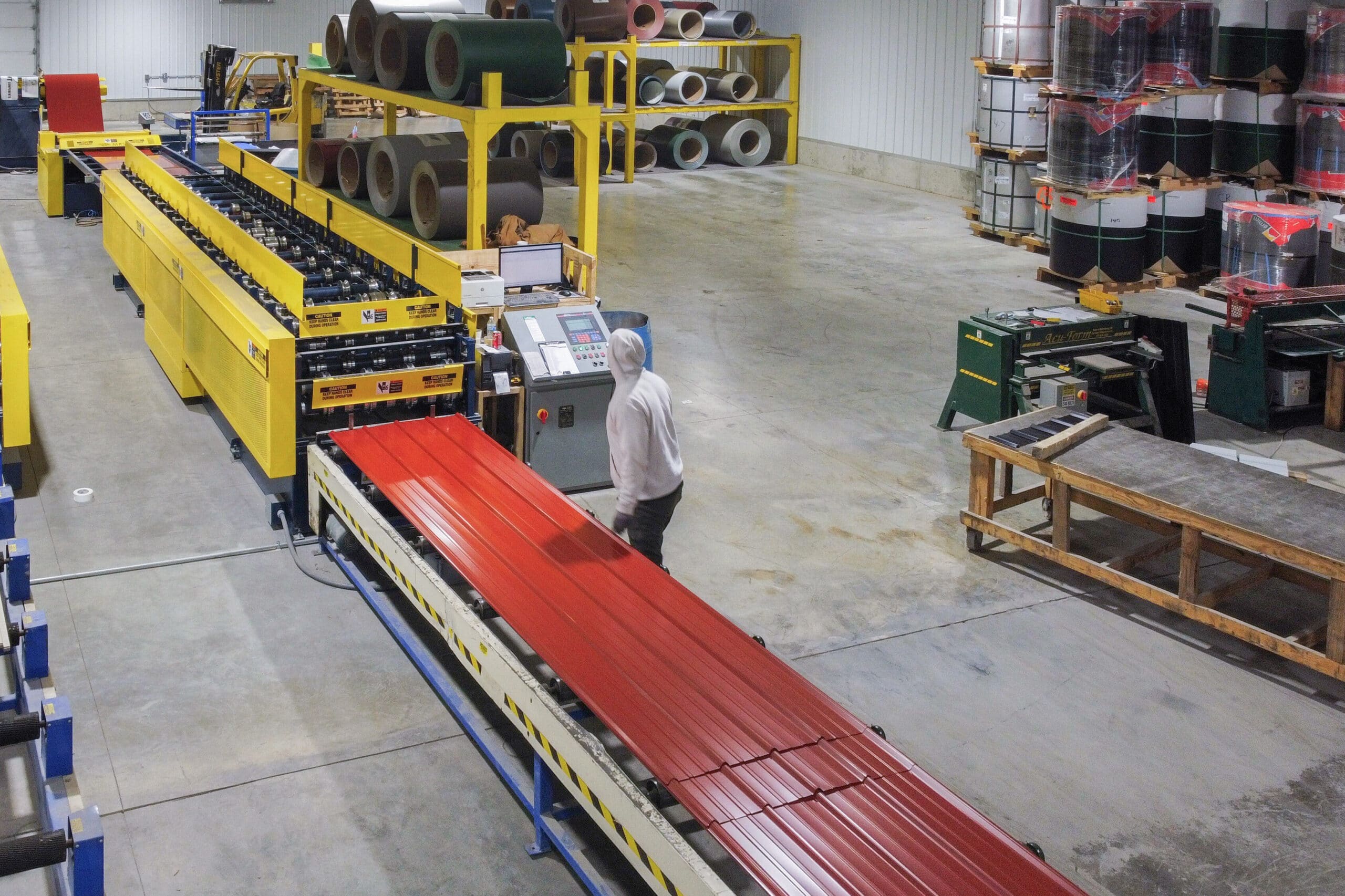 man manufacturing red metal panels from a yellow machine