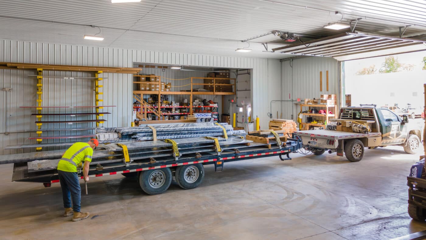 man strapping on metal panels to trailer attached to green truck so it is ready for delivery