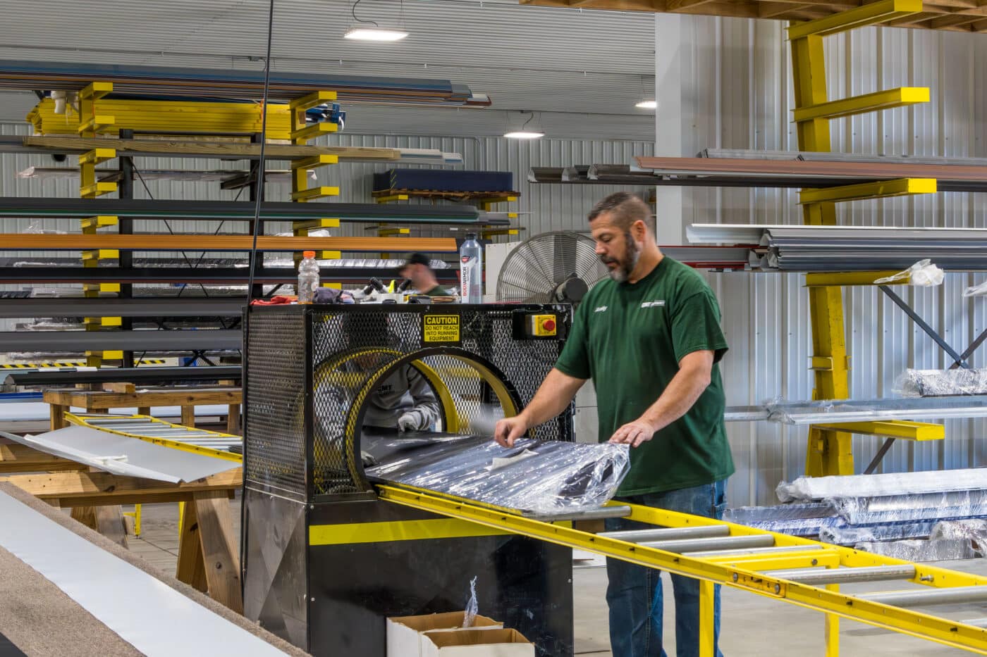 man wrapping and placing sticker on metal panels for a 24x32 pole barn garage kit as it comes out of yellow and black machine
