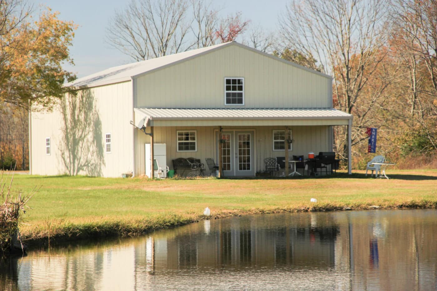 off white metal pole barn with tan trim and metal roofing featuring a porch overlooking a body of water