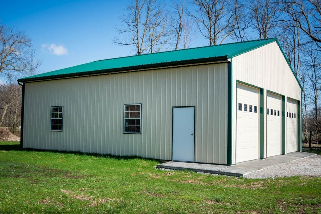 white pole barn garage with green trim and green roof with three garage doors in McArthur OH