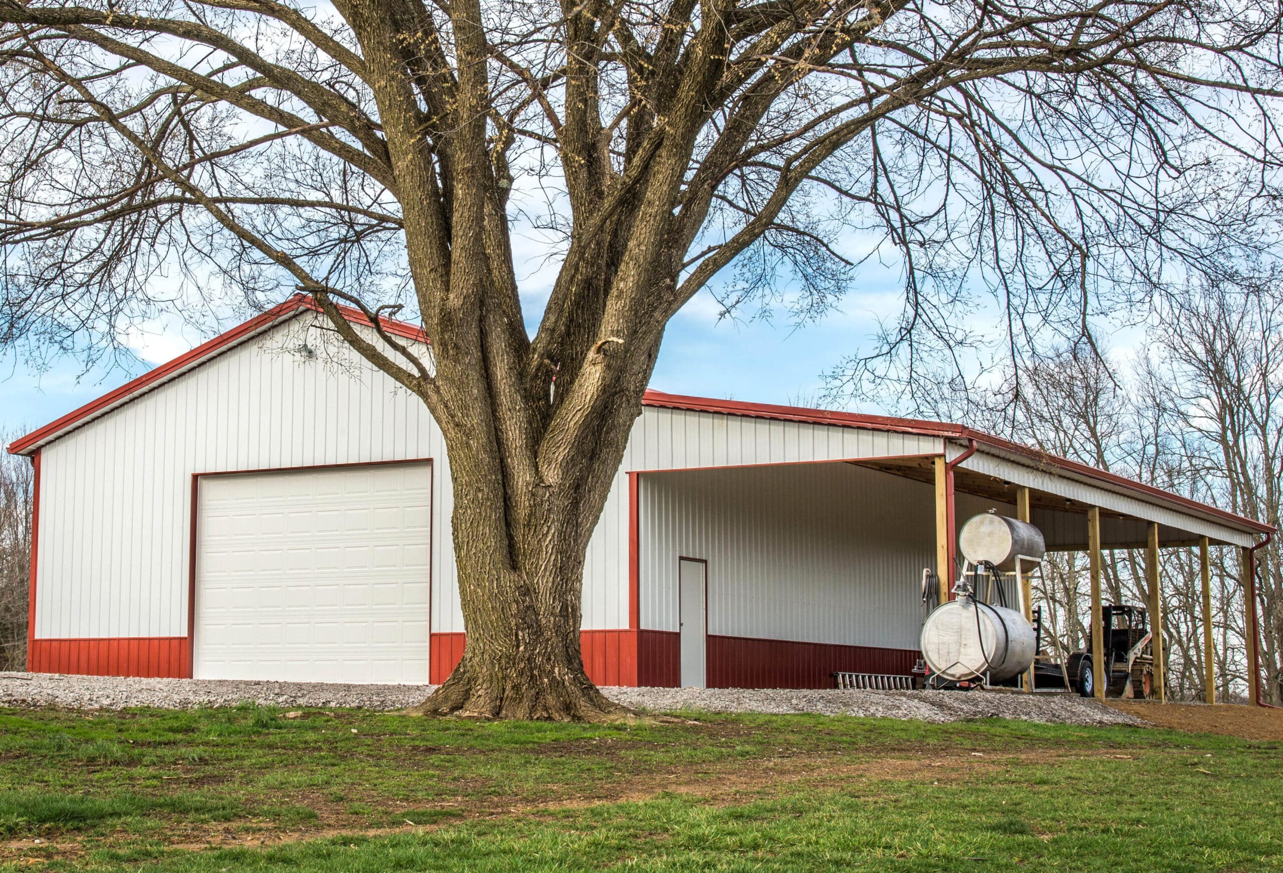 red and white 40x64 agricultural pole barn with farm equipment under the front roof