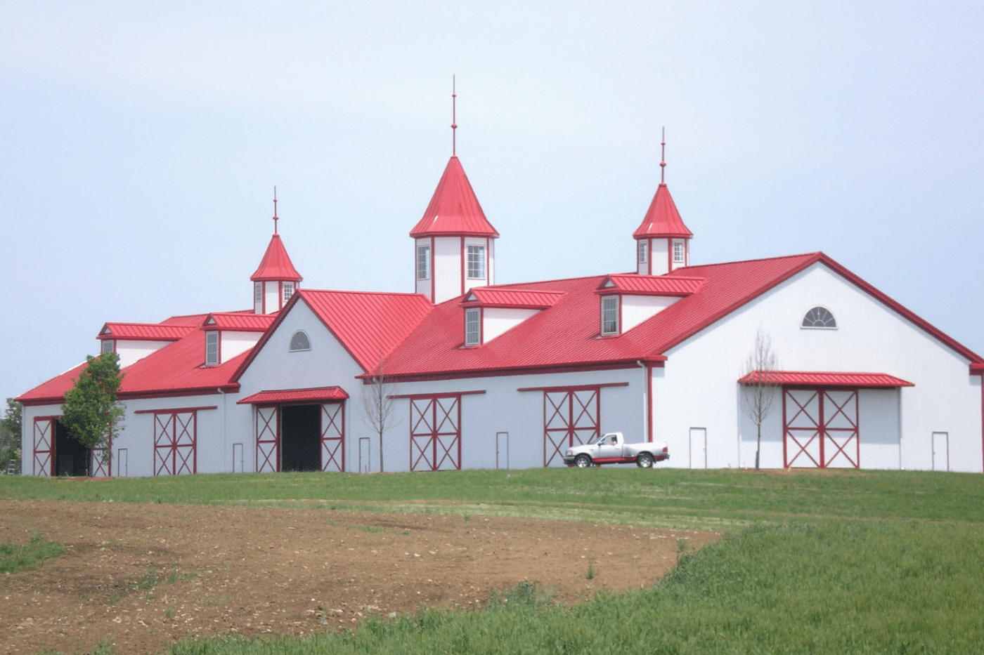 red and white 80x120 equestrian pole barn kit with doors and car outside