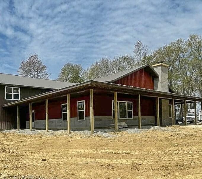 red metal siding on commercial pole barn with brown metal sided building attached featuring overhang and stone chimney