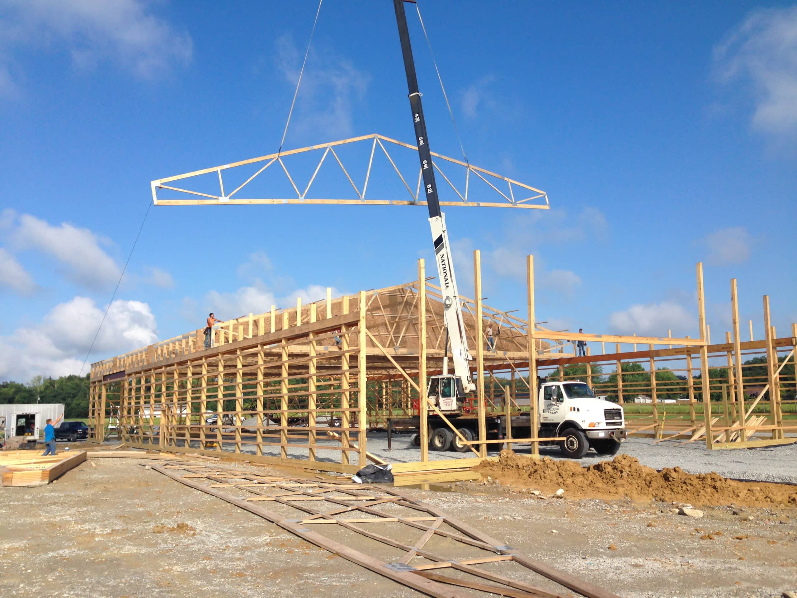 roof truss being lowered onto frame of pole barn kit in Norwood