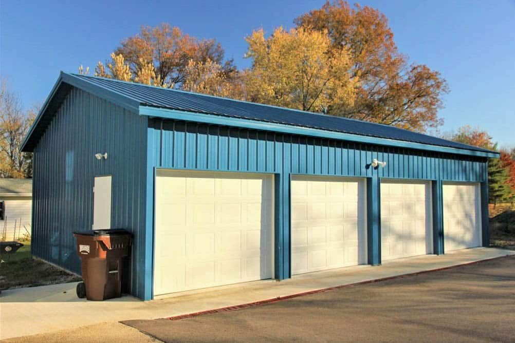 side angle of blue pole barn garage with 4 white overhead doors