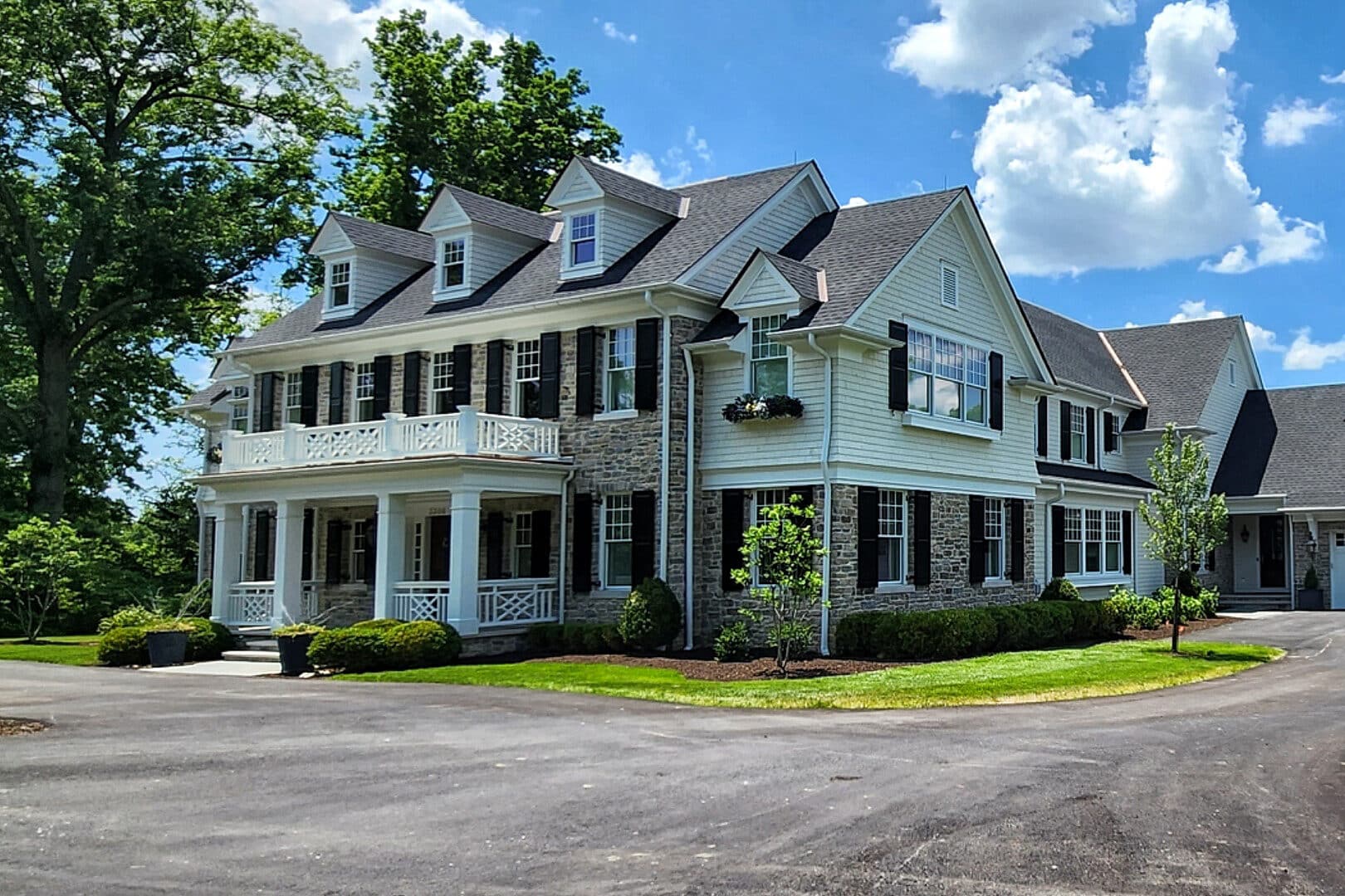 stone barndominium with white siding featuring two stories with upper balcony as well as attached three car garage with transom windows