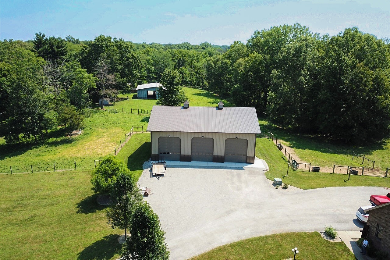 tan and gray three car pole barn garage with three brown overhead doors and two cupolas on a brown metal roof