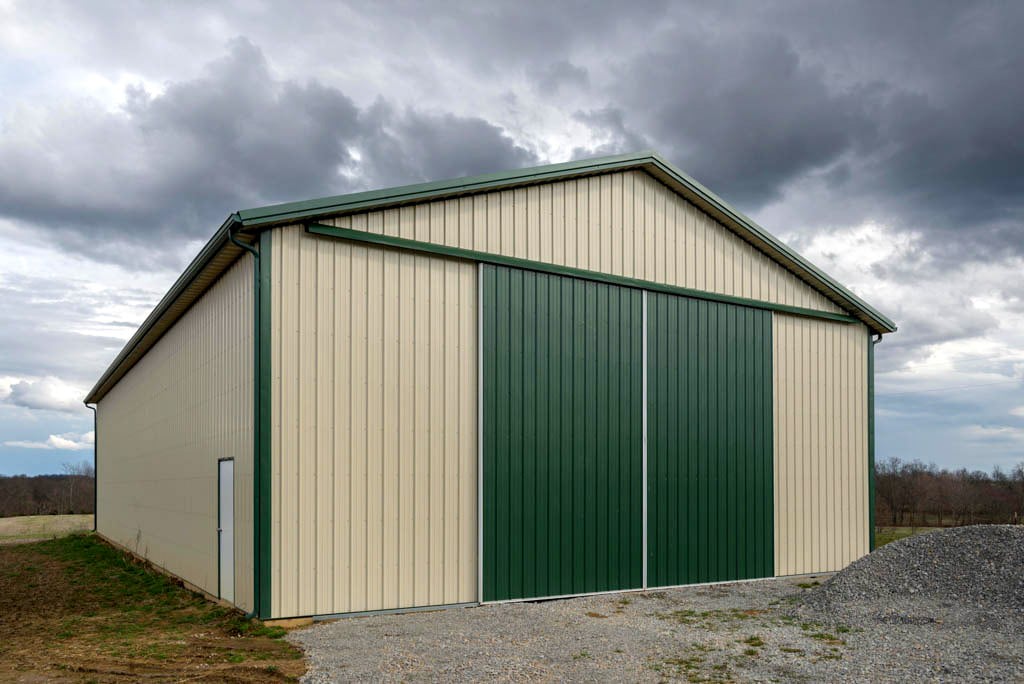 tan pole barn kits in Buford Oh with green metal slider doors and green trim featuring white side door