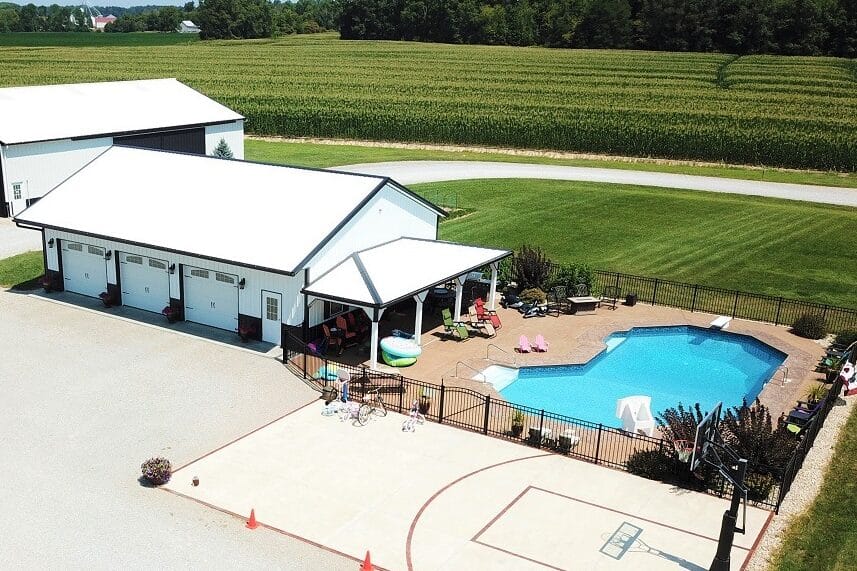 three car white and black pole barn garage with side overhang extending over a pool